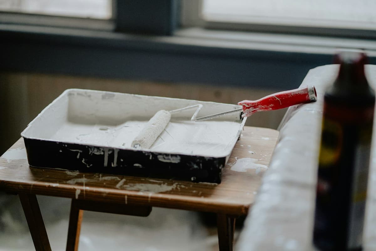 A paint roller with a red handle in a tray of white paint
